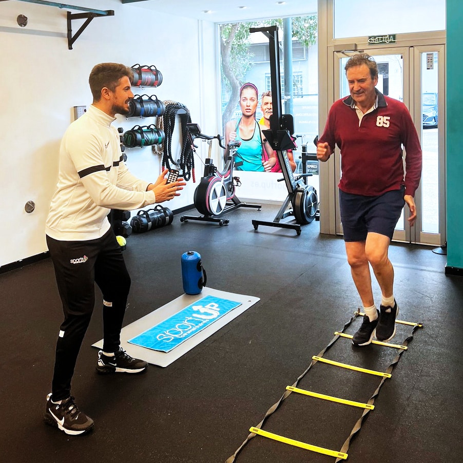 Entrenador animando a un señor haciendo una ejercicio con una escalera de agilidad